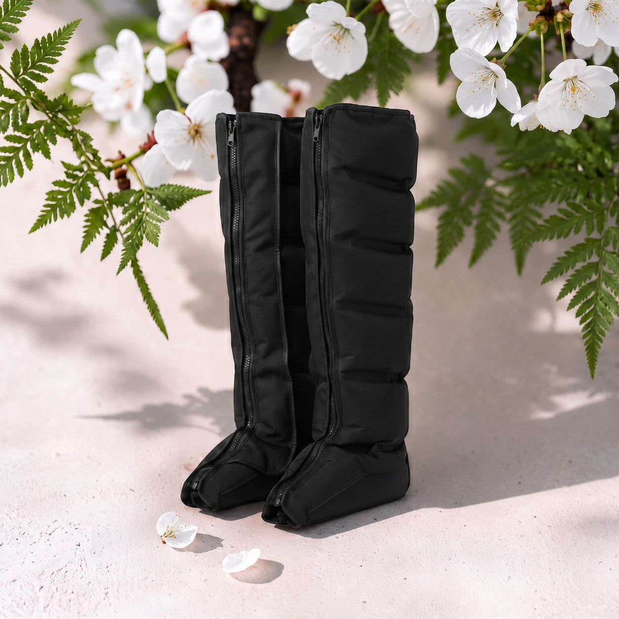 Mole Luxe siyah renkli, fermuarlı, hava kompresyonlu bacak masaj botları, çiçekli bir arka plan üzerinde duruyor.